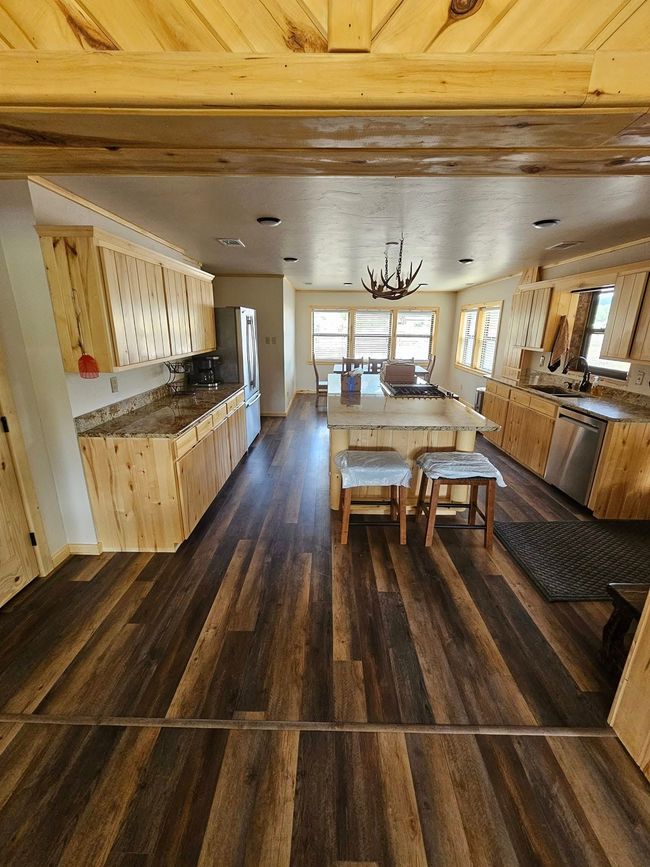 Spacious kitchen with light wood cabinets, dark wood floor, and an island with stools; dining area in the background.