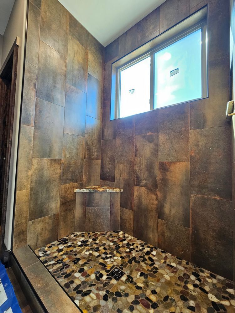Brown tiled shower with pebble floor, window, and built-in shelf.