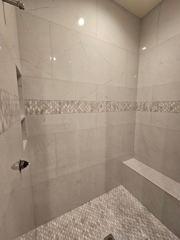 Tiled shower with grey stone, mosaic band, built-in bench, and recessed shelves.