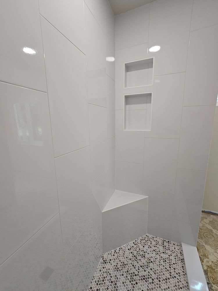 White tiled shower with corner bench, two built-in shelves, and mosaic floor.