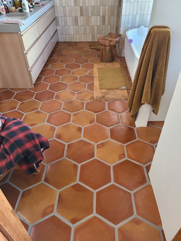 Bathroom with reddish-brown hexagonal tiles, a tub, and a towel draped over the wall.