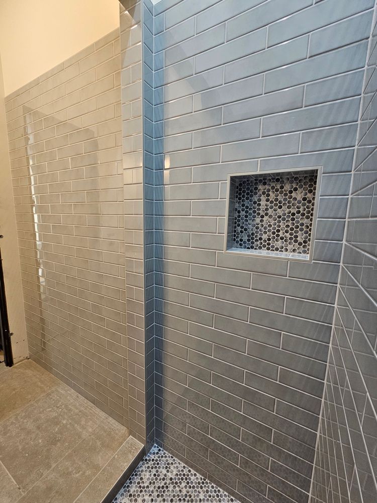 Gray tiled shower with a mosaic-tiled inset, viewed from a corner.