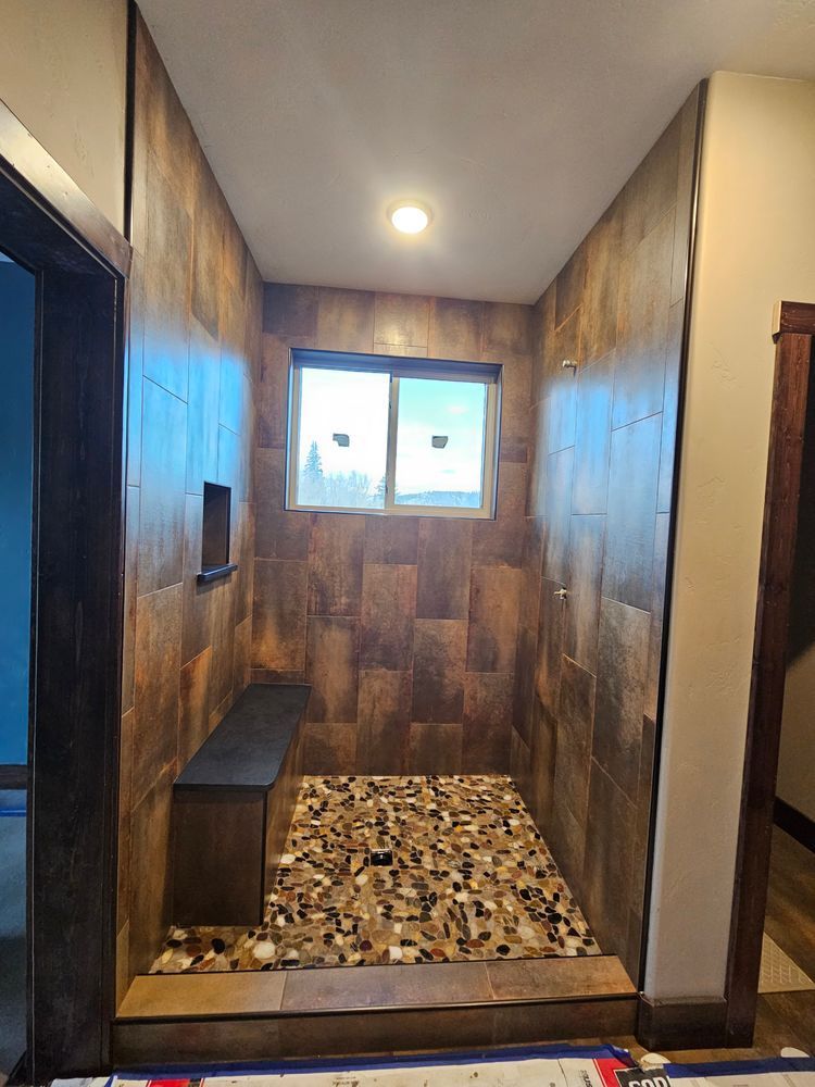 Shower with brown tile walls, stone floor, built-in bench, and small window.