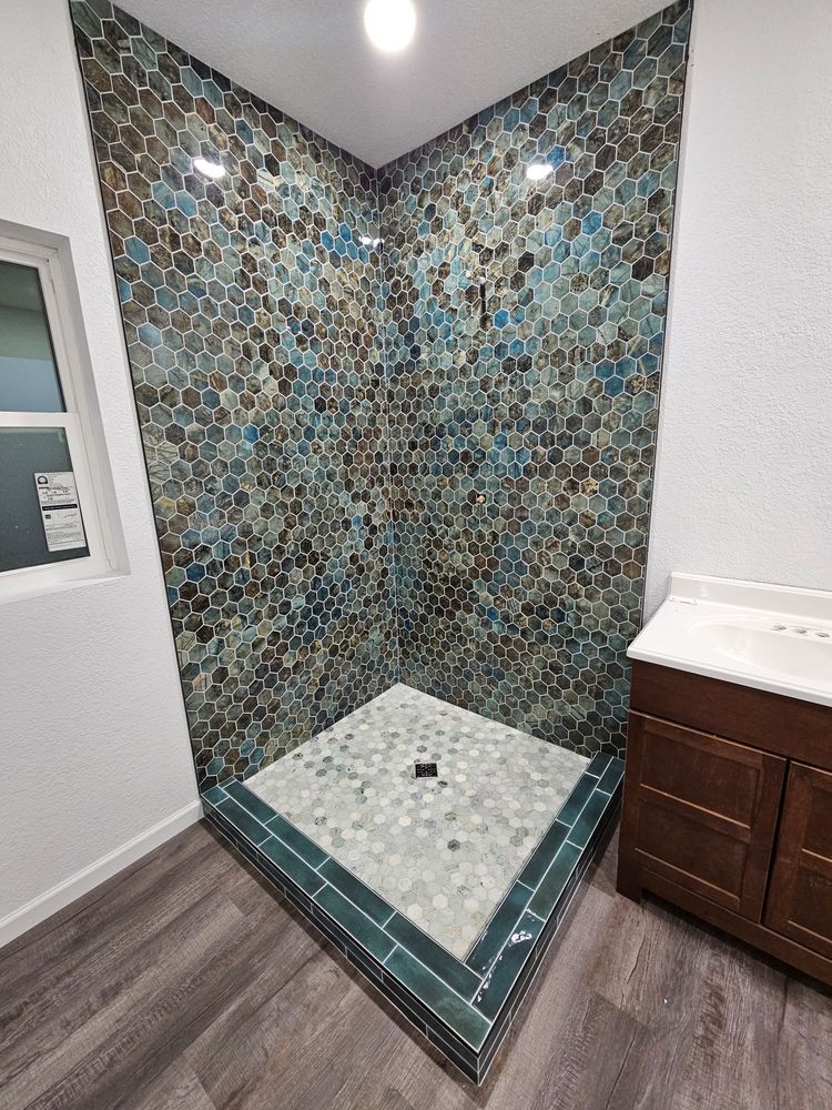 Corner shower with patterned blue, brown, and gray tile, white vanity, and wood-look flooring.