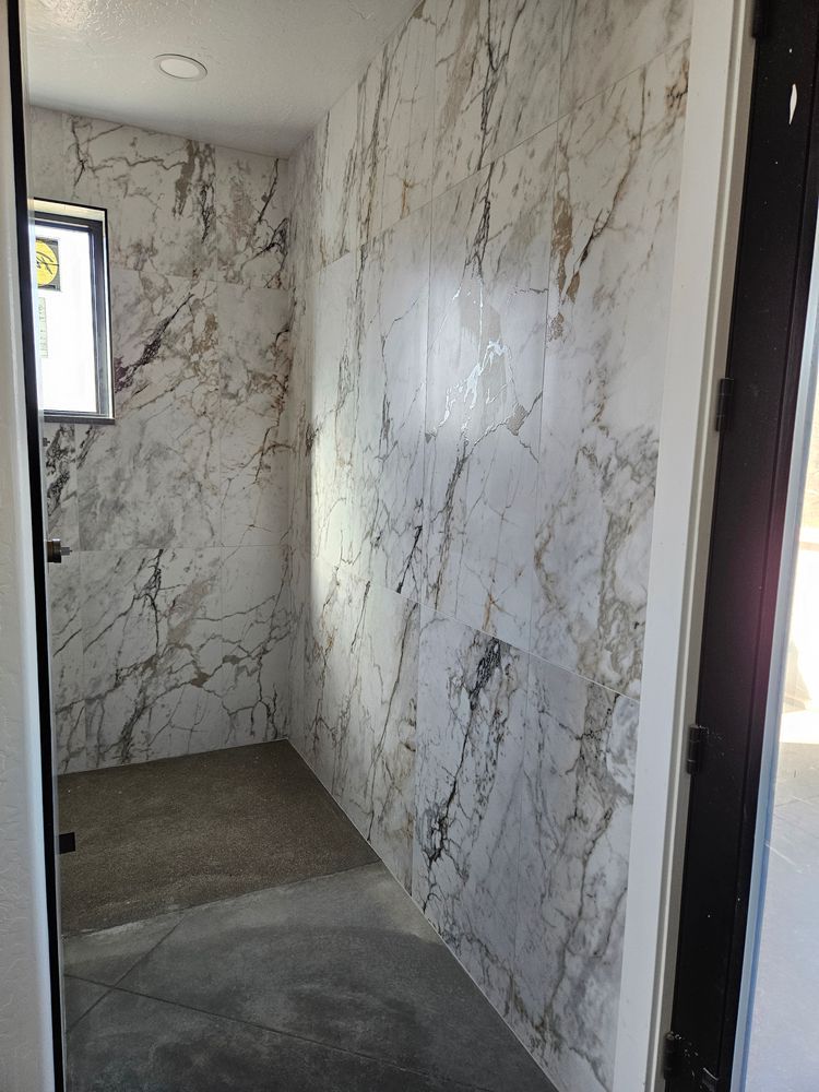 Bathroom with marble-patterned walls, unfinished concrete floor, window, and open doorway.