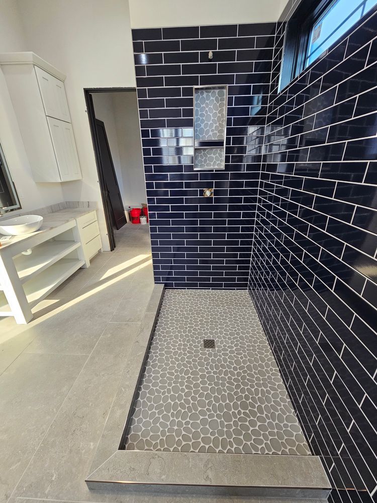 Modern bathroom with black tiled shower, gray pebble floor, and white vanity.