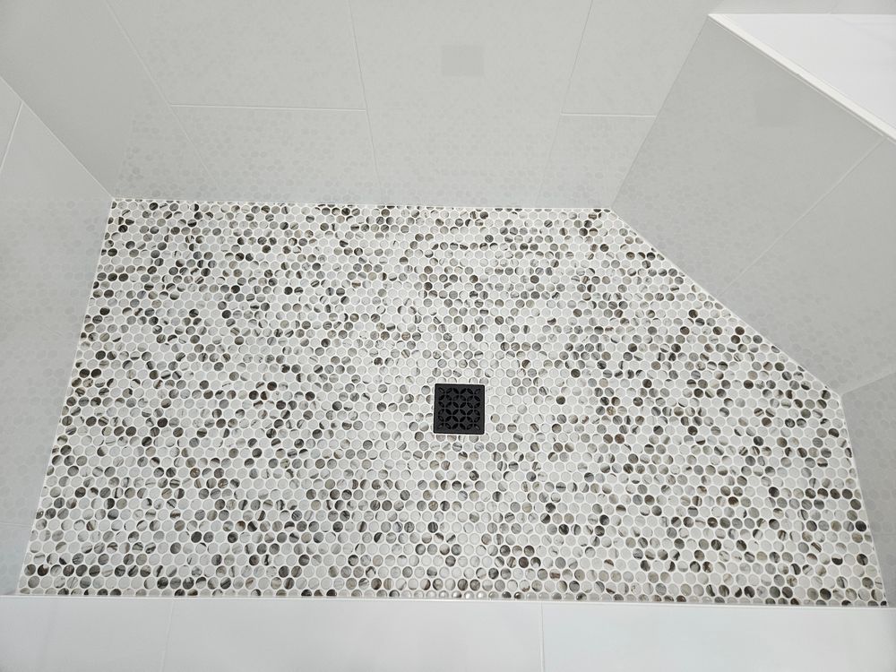 Shower with mosaic tile wall, white walls, and black drain.