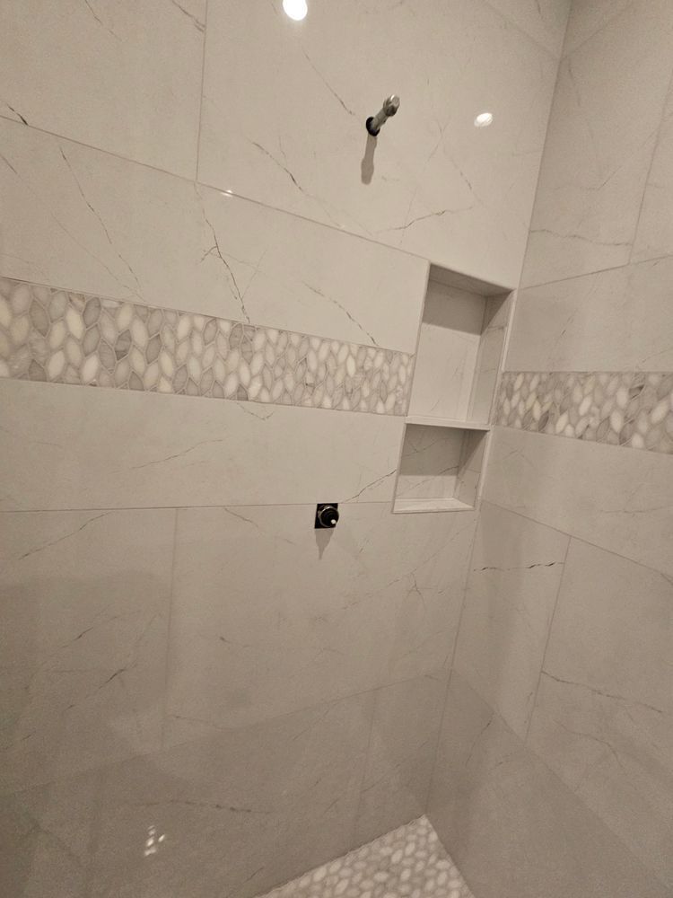 White tiled shower with decorative band and recessed shelves.