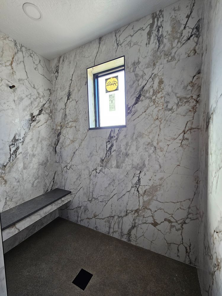 Marble-tiled shower with a dark bench, window, and dark floor.