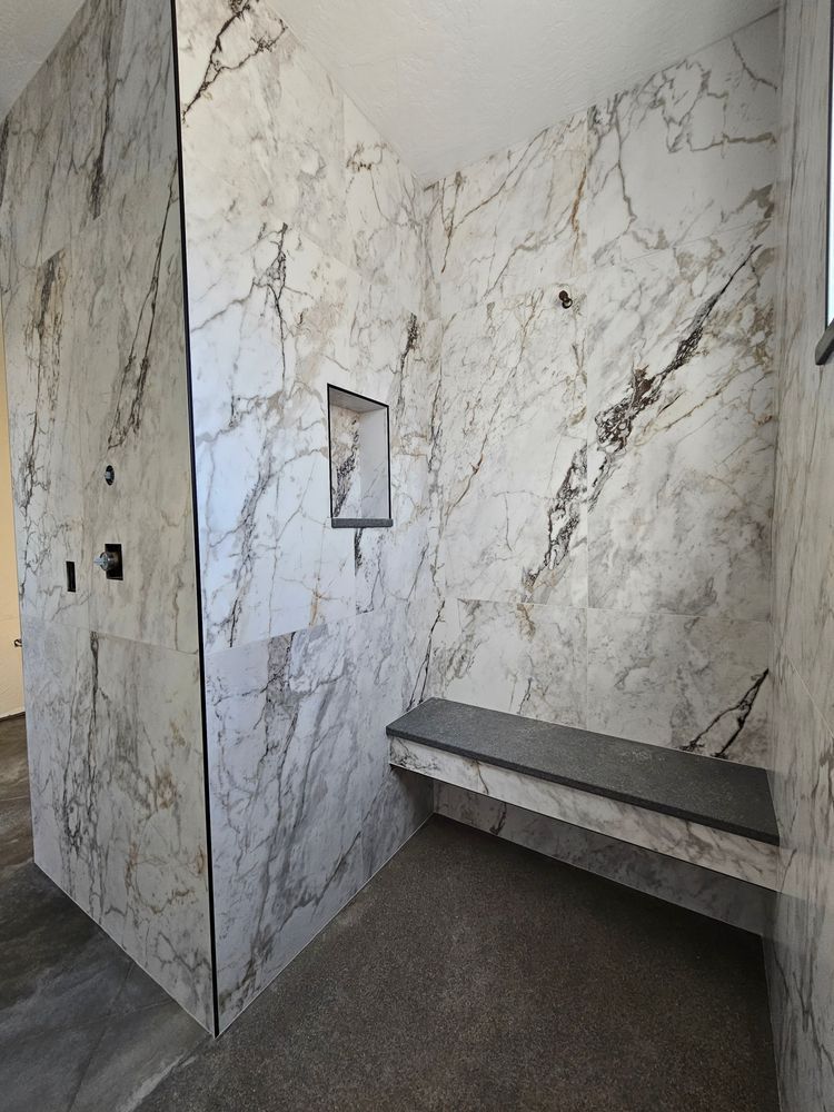 Marble-tiled shower with built-in bench and recessed shelf; neutral tones.