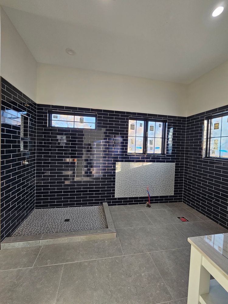 Bathroom under construction with black tiled walls, pebble shower floor, and windows.