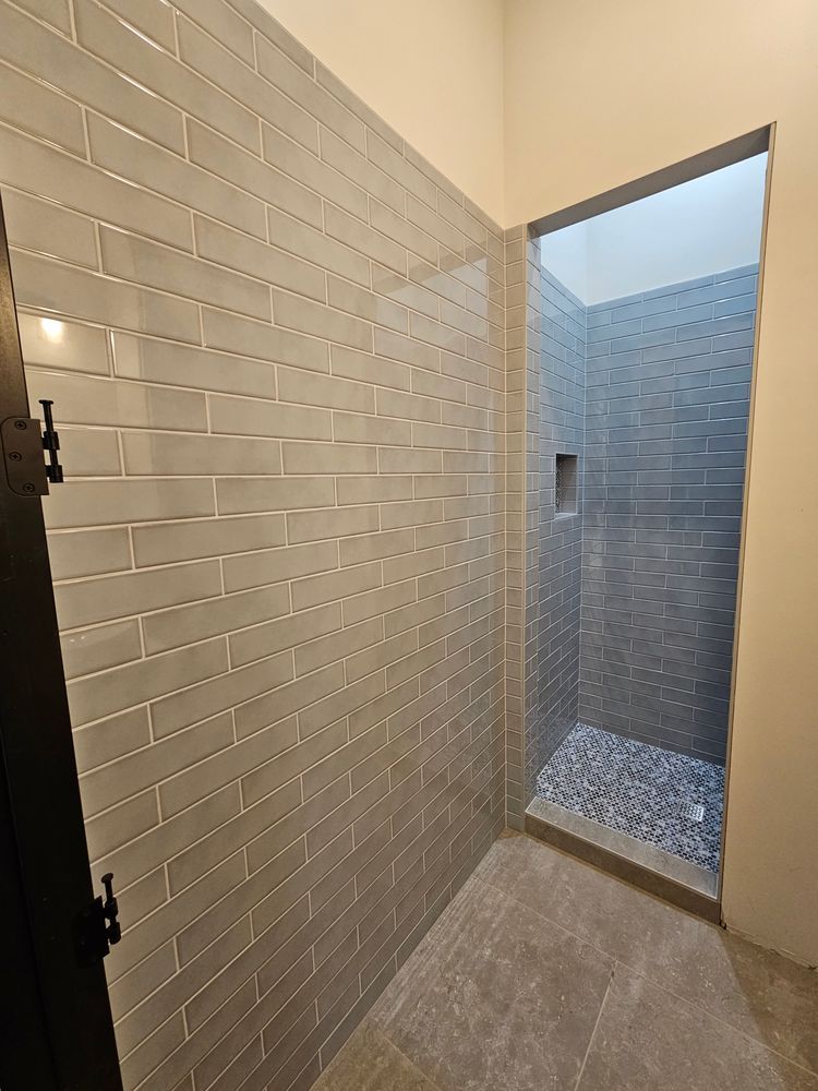 A modern shower with gray brick-patterned tiles and pebble floor.