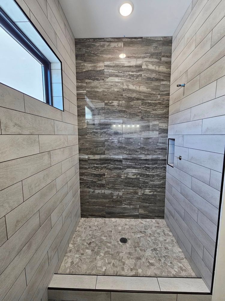 Modern shower with gray and white tile, stone floor, and a small window.