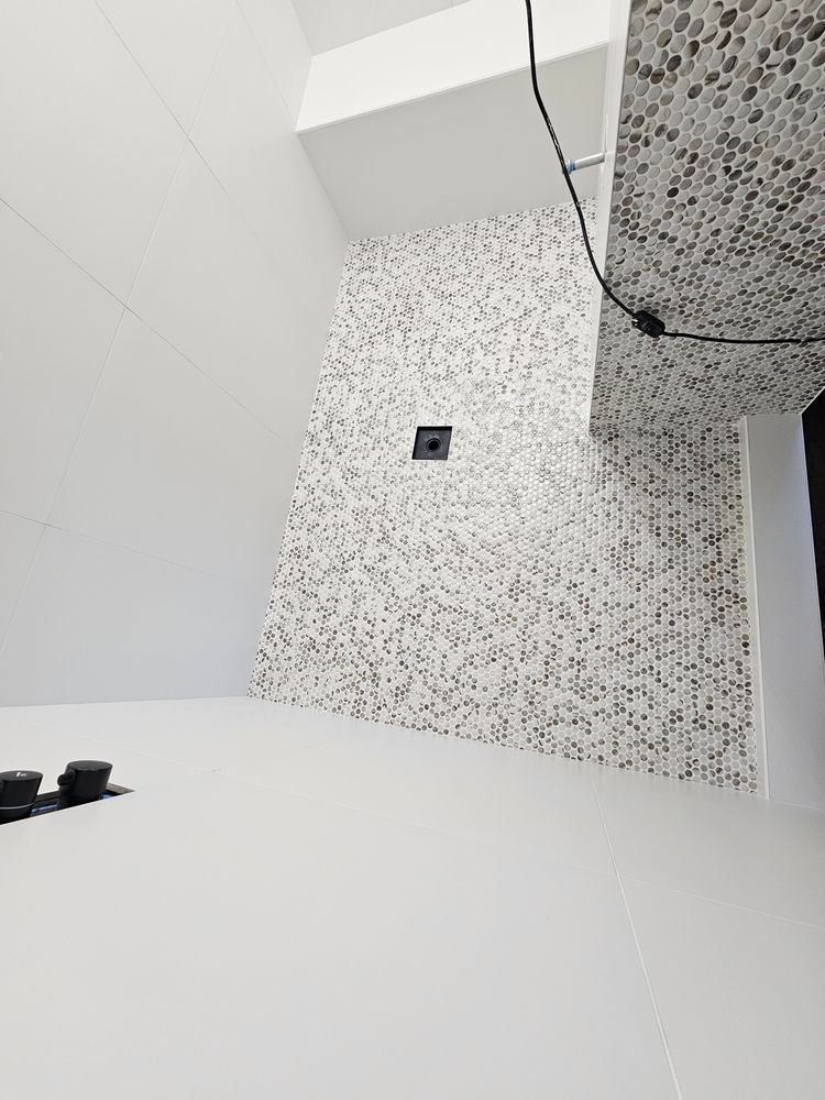 White and mosaic tile shower with black fixtures; corner view.