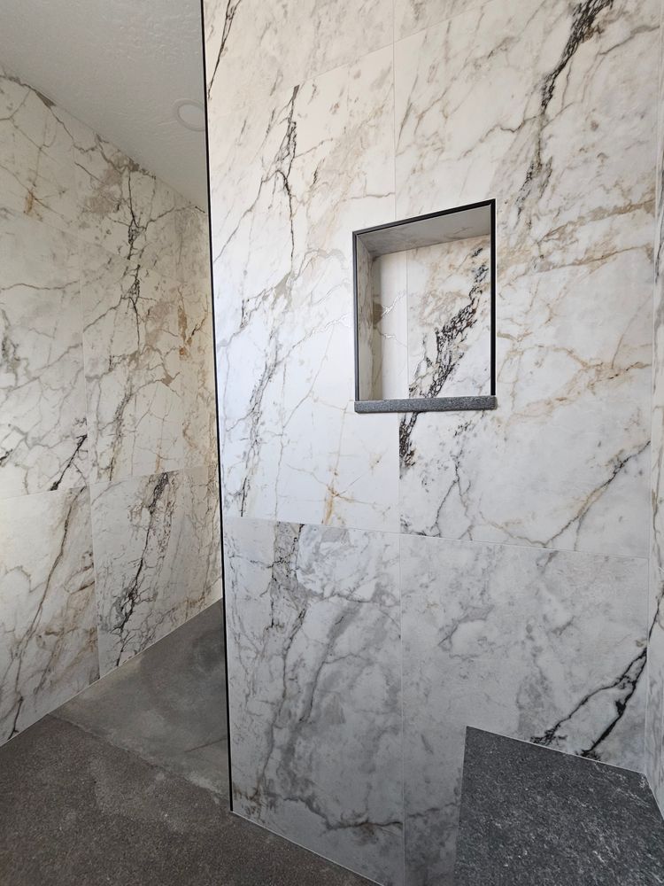 Shower walls tiled with white marble, a built-in shelf, and a gray floor.