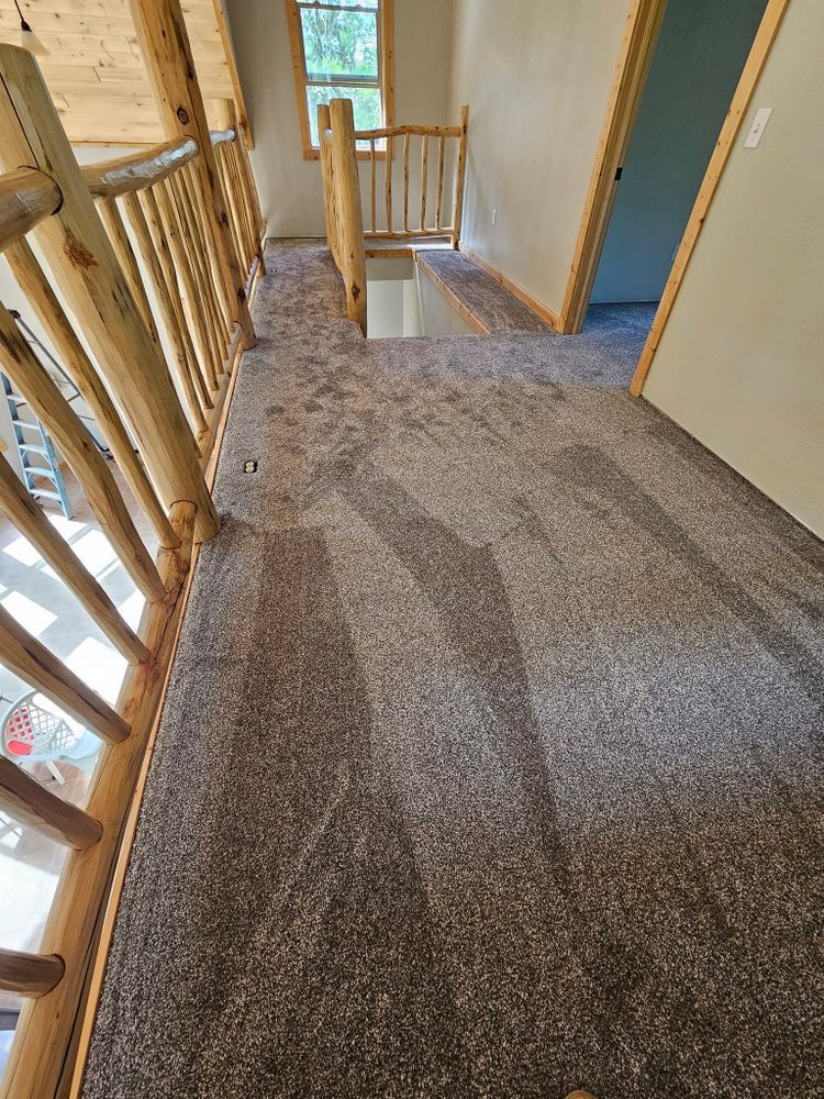 Hallway with light brown carpet, log railings, doorway, and natural light from a window.