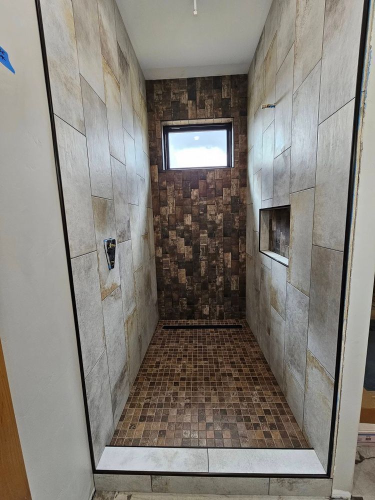 Shower with brown, beige, and mosaic tiles, recessed shelf, and small window.