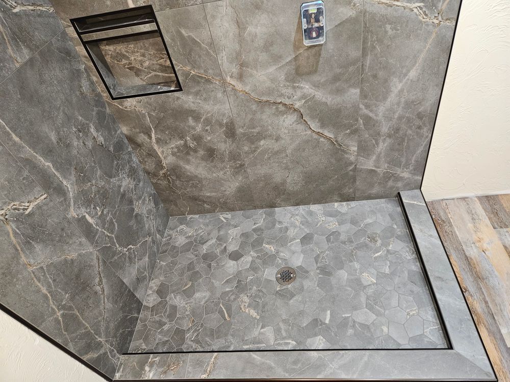 Gray tiled shower with built-in shelf and decorative floor.