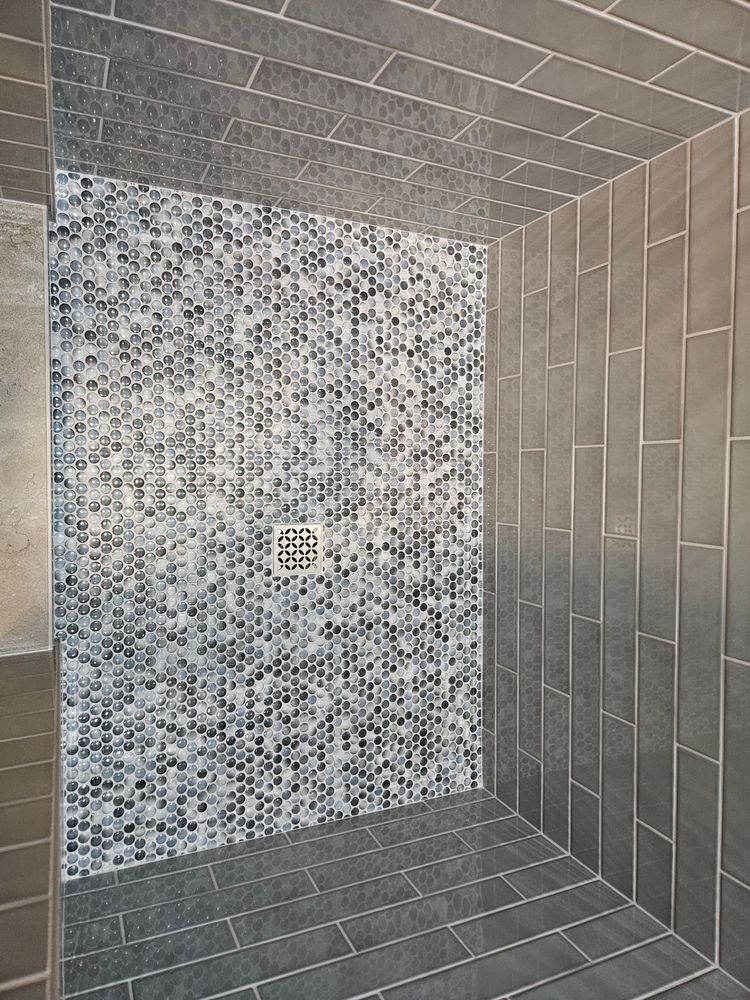 Gray tiled shower with a mosaic-tiled back wall and a metal drain.