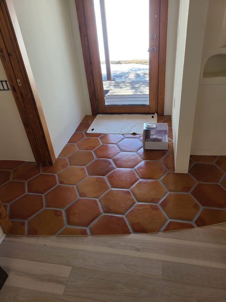 Hexagonal terracotta tiles in an entryway with a wooden door. Light enters the room.