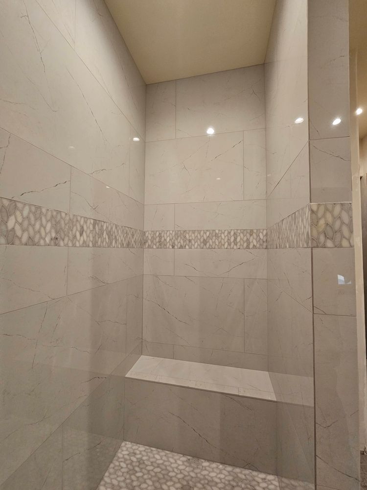 Tiled shower with a built-in bench and decorative band; light gray and white tones.
