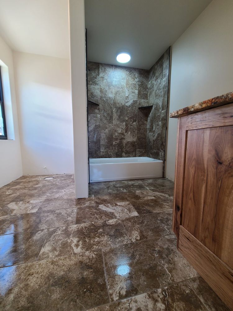 Bathroom with brown tiled floor, white walls, and a shower with brown stone-like tiles.
