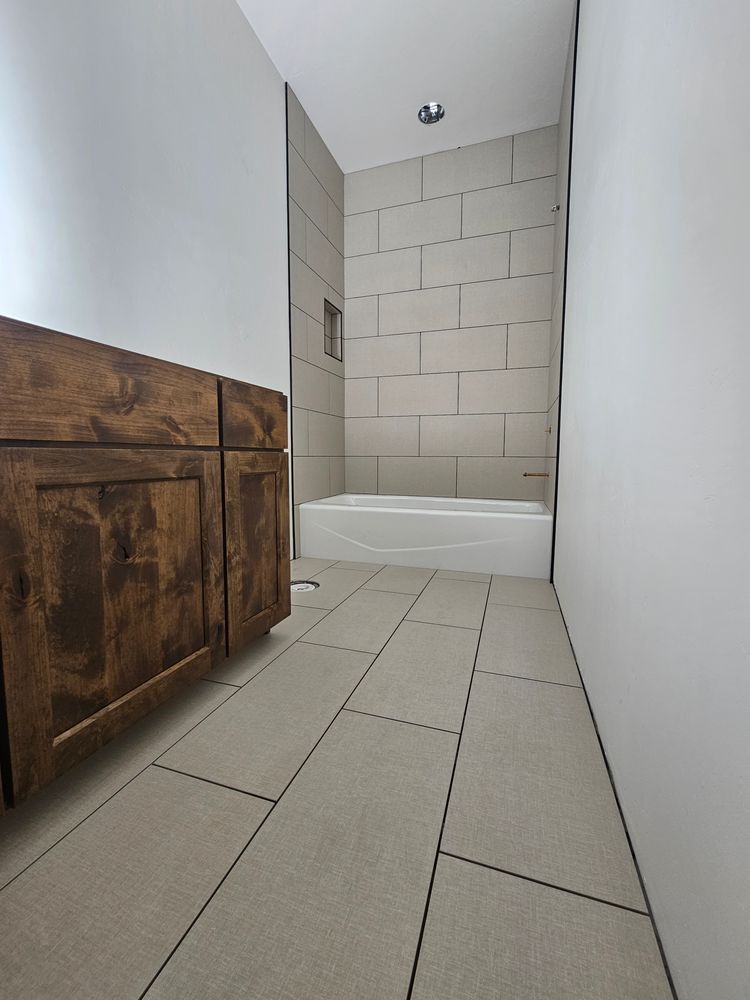 Bathroom with wooden cabinets, tiled floor, and a bathtub with tiled walls.