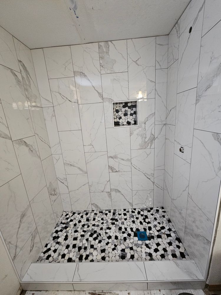 Shower stall with marble-patterned walls, black and white tiled floor, and a small inset shelf.