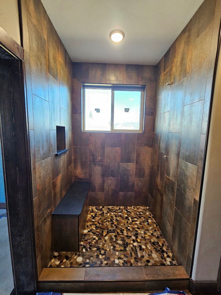 Shower with brown tile walls, pebble floor, and a built-in bench. Window in the center.