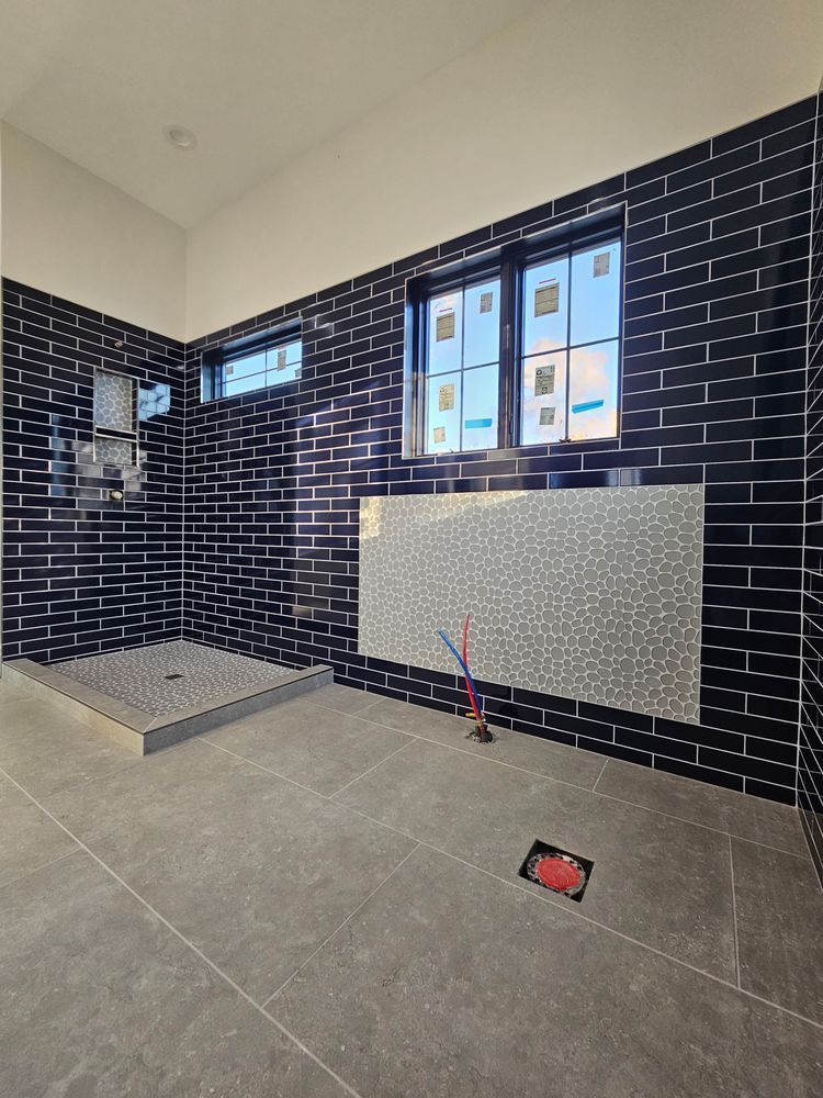Modern bathroom with black tiled walls, gray floors, and a silver mosaic accent.