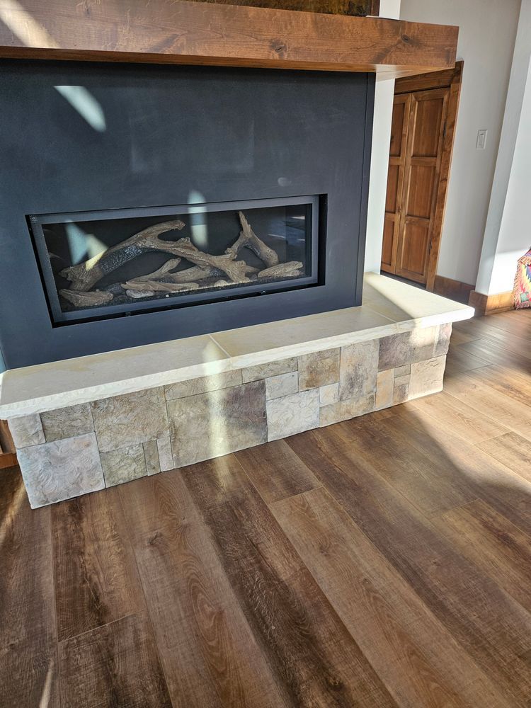 Fireplace with faux wood logs, dark surround, and stone facade, resting on wood-look flooring.