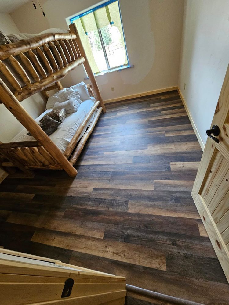 A bedroom with a wooden bunk bed, hardwood floors, and a window; the door is also wooden.