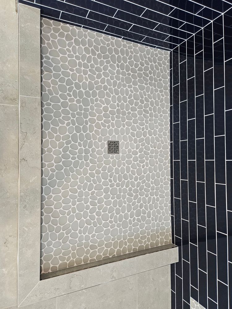 Shower with gray pebble tile floor, blue subway tile walls, and a metal drain.