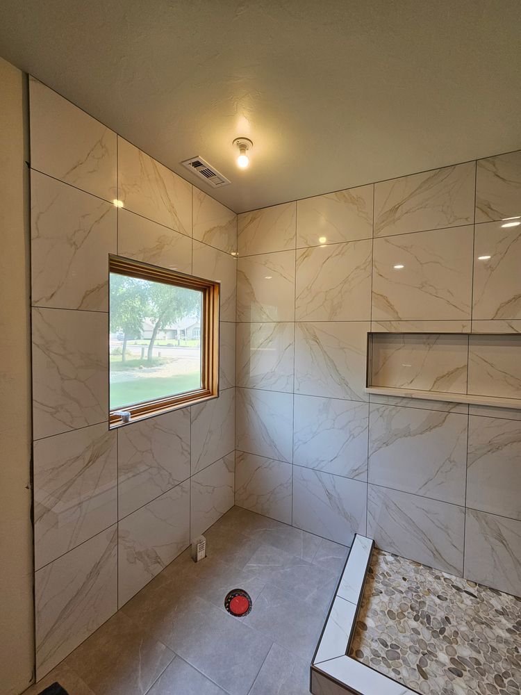 Bathroom interior with marble-look tile walls, window, built-in shelf, and unfinished floor.