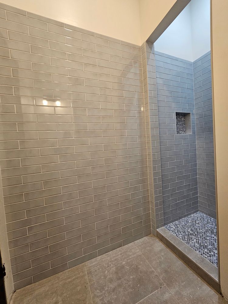 Gray tiled shower with a recessed niche, pebble floor, and glass door.