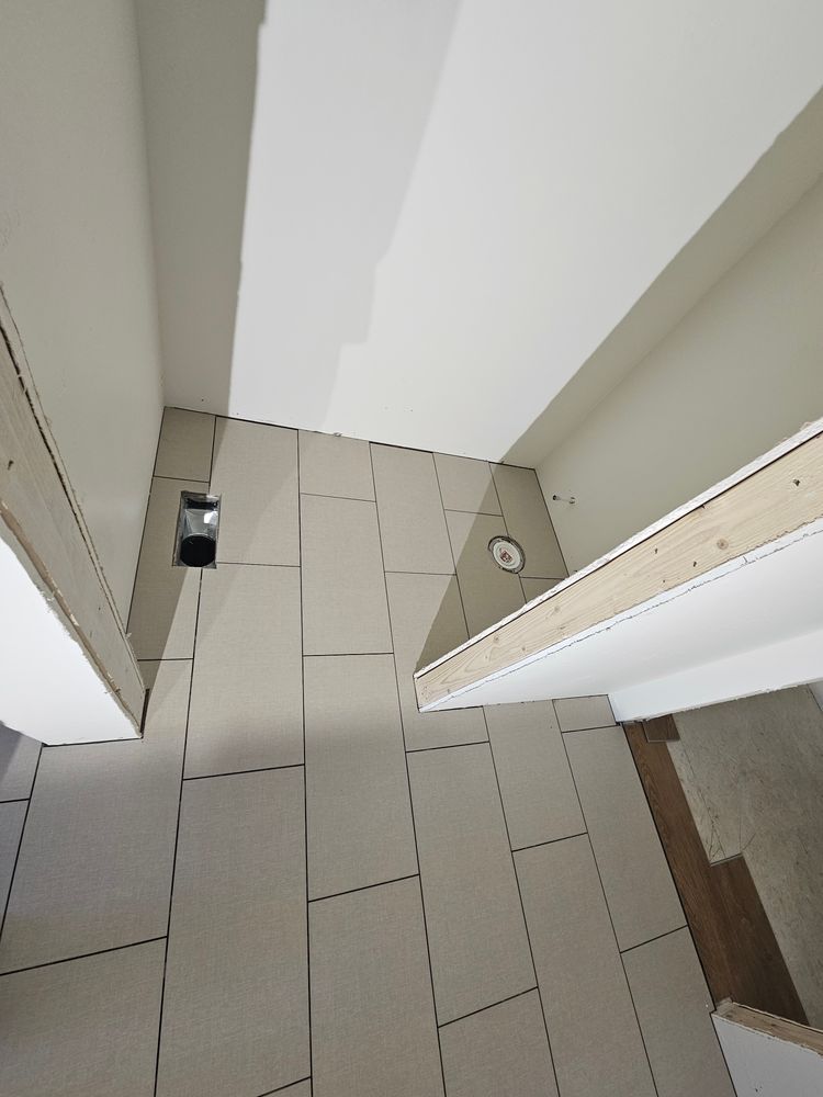 Bathroom floor with light-colored tiles, a drain, and unfinished walls; overhead view.