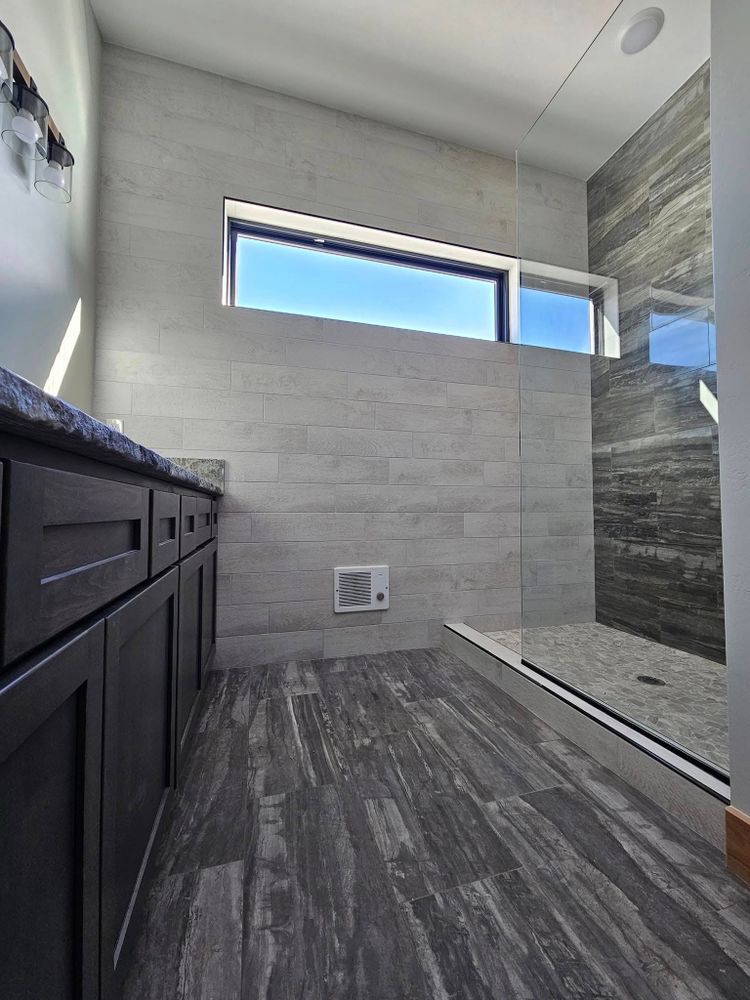 Modern bathroom with gray and black tones, a shower, window, and vanity.
