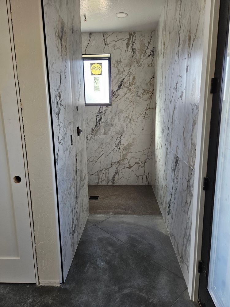 Narrow hallway with marble-tiled shower, concrete floor, and a window at the end.
