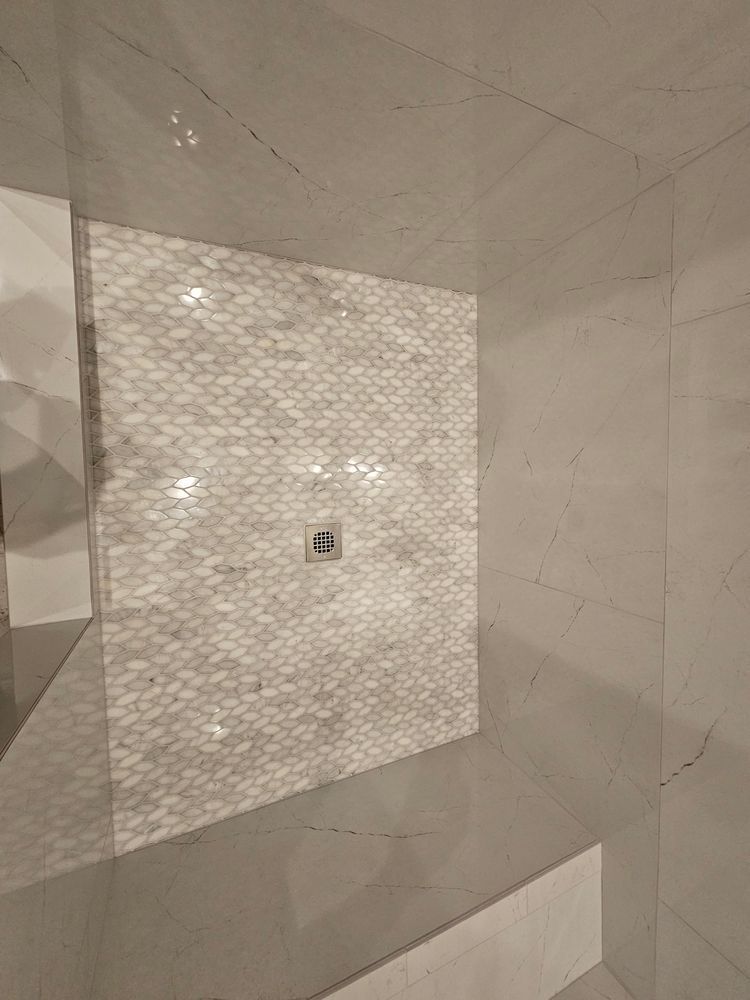 Bathroom shower with patterned tile accent wall and drain, surrounded by smooth, light gray tiles.