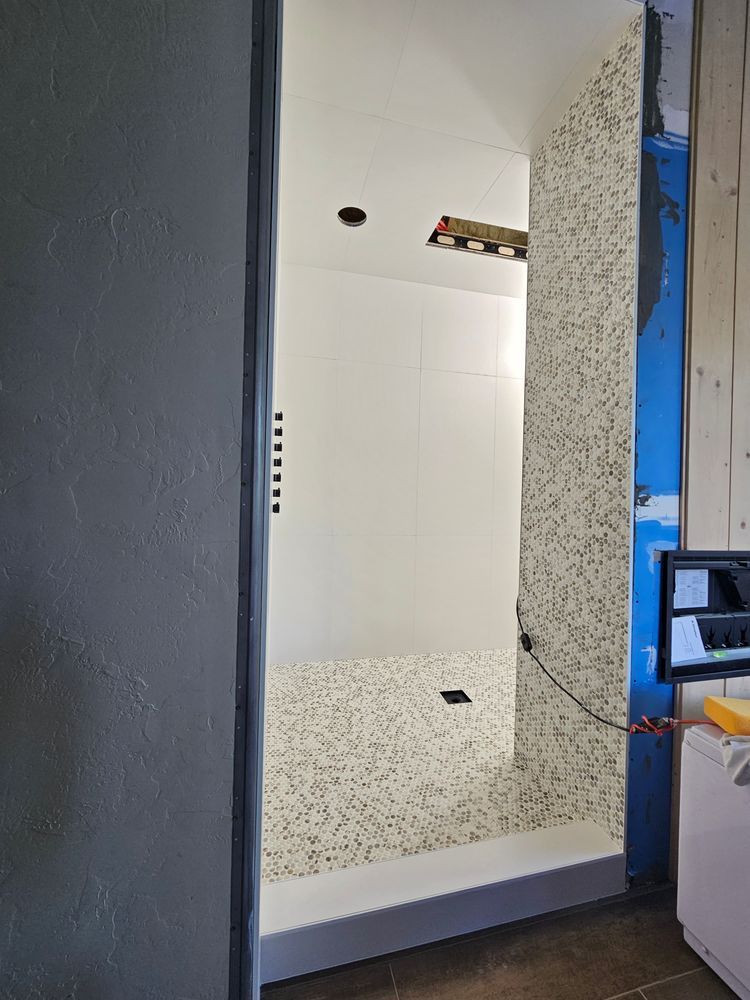 Shower under construction: white walls and mosaic tile floor; blue framing visible.