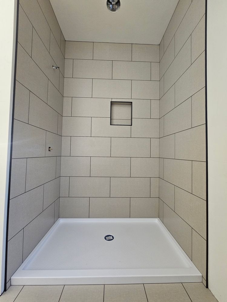 Shower stall with white tile walls, a built-in shelf, and a white base.