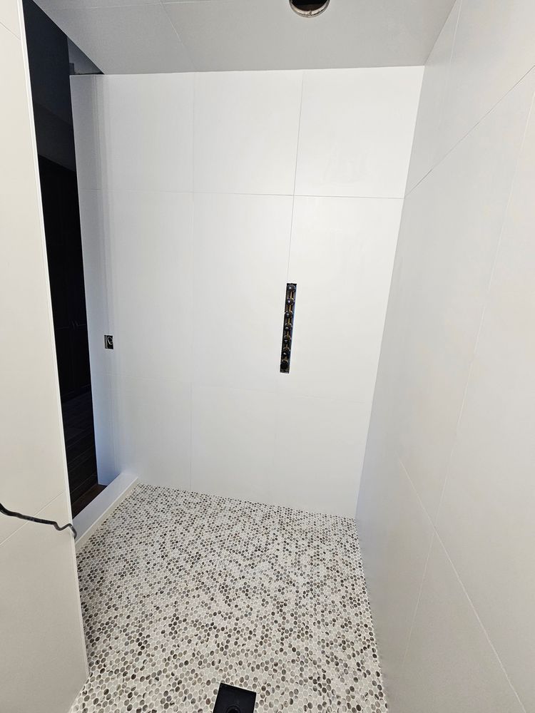White tiled shower with mosaic floor, glass door, and dark fixture.