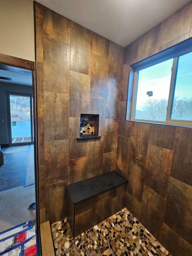 Brown tiled shower with a bench and window, stone floor. A small shelf is built into the wall.