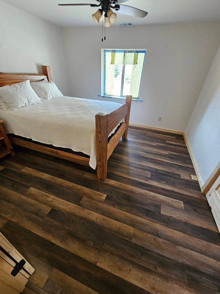 Bedroom with a wooden bed, white bedding, and dark wood flooring. Window with blue trim and a ceiling fan.