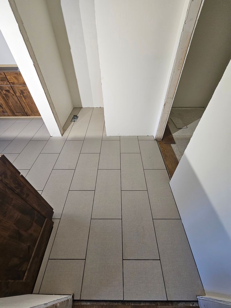 Looking down a hallway with light gray rectangular tiles, white walls, and a dark wooden door.