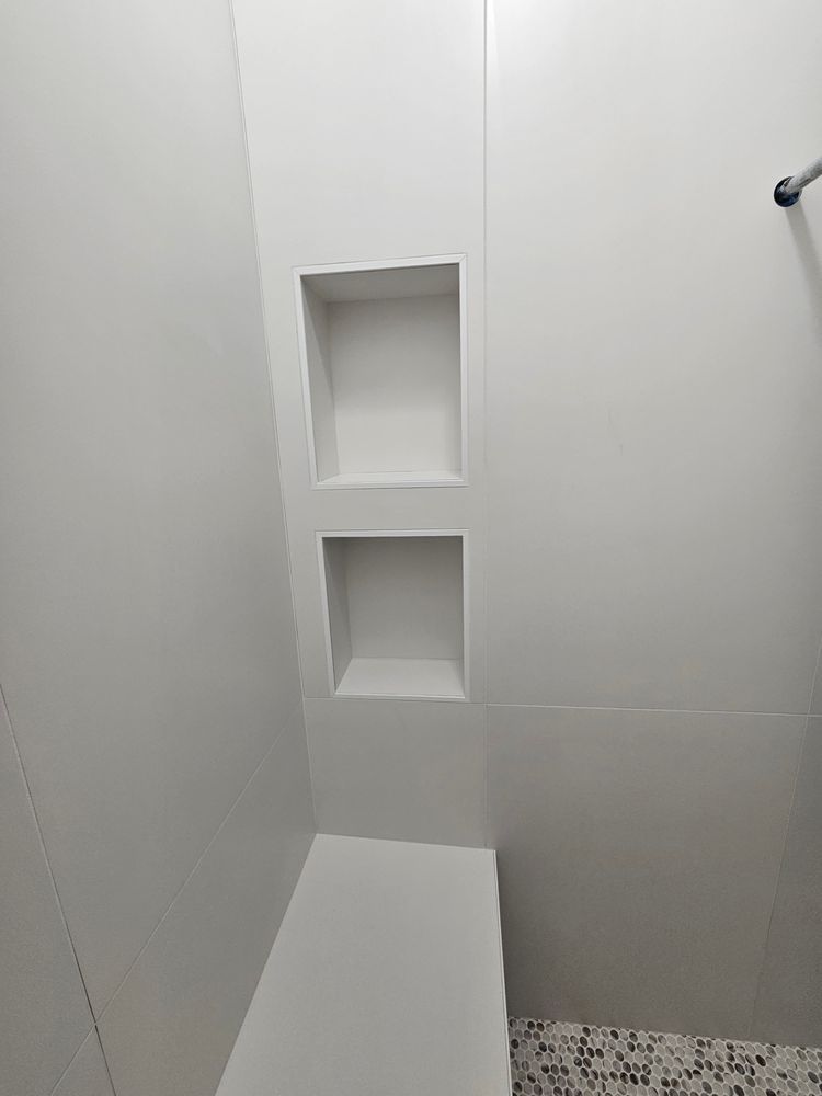 White tiled shower with two recessed shelves and a built-in seat.