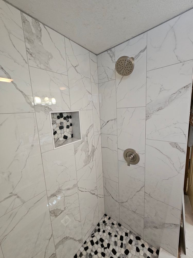 White marble-tiled shower with pebble floor, niche, and silver shower fixtures.