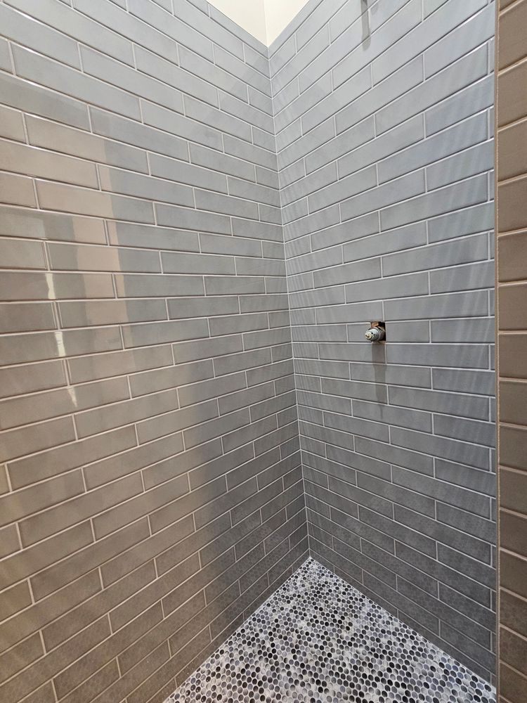 Gray tiled shower with pebble floor; chrome showerhead.