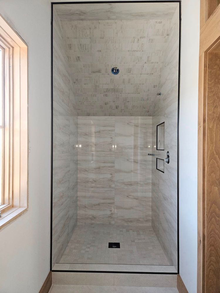 A walk-in shower with light-colored tile walls and floor, framed by black trim and clear glass.