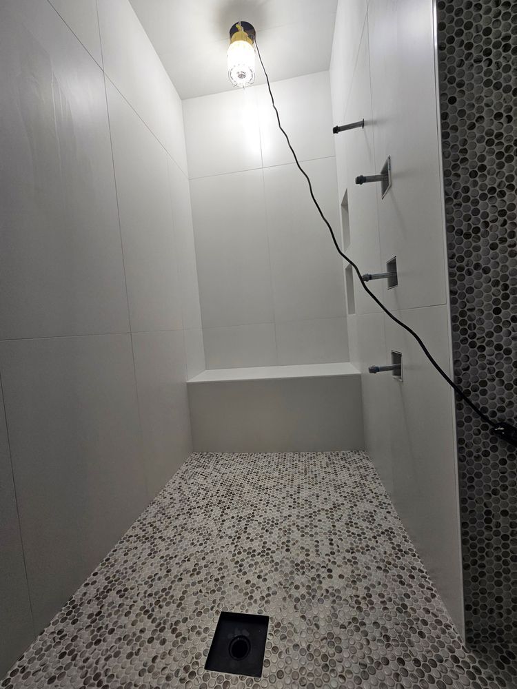 Shower stall with white tiled walls, mosaic floor, and an exposed light fixture.